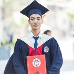 Proud graduate in academic gown holding diploma, celebrating academic success.